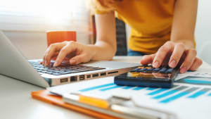 Personne travaillant sur ordinateur avec une calculatrice et graphiques.