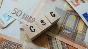 Acronyme CSG fait de cubes de lettres en bois sur une pile de billets de banque en euros. Contribution Sociale Généralisée, une taxe finançant la sécurité sociale