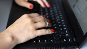 Mains féminines sur le clavier d'un ordinateur portable noir sur un bureau. Femme avec une manucure rouge tapant du texte, travaillant avec des documents.