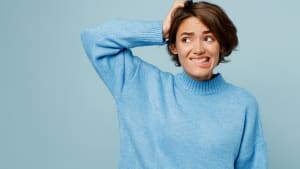 Jeune femme caucasienne triste portant un pull tricoté disant oups isolée sur un fond de studio bleu clair pastel uni.