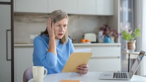 Une femme �g�e se couvrant l'oreille et paraissant anxieuse en lisant une facture.