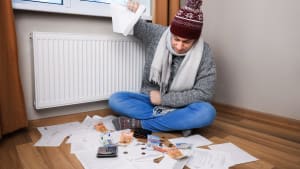 Un homme en  v�tements d'hiver assis pr�s d'un radiateur avec des factures et de l'argent.