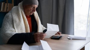 Un homme âgé ouvrant une facture d'énergie avec inquiétude, enveloppé dans une couverture.