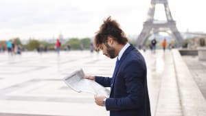 Homme en costume lit un journal devant la tour Eiffel.