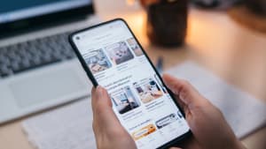 Personne cherchant un logement sur une application mobile, ordinateur derrière.
