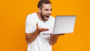 Portrait d'un homme criant et tenant un ordinateur portable.