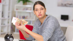 femme tenant des billets de banque d'une tirelire et soupirant de frustration