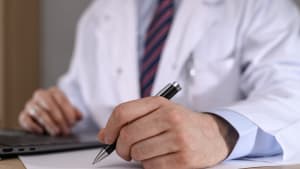 Un médecin tenant un stylo, écrivant quelque chose sur un morceau de papier, rédigeant une ordonnance ou une référence.