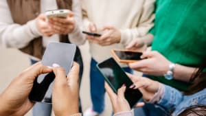 Plusieurs personnes tiennent et utilisent des smartphones ensemble dehors.