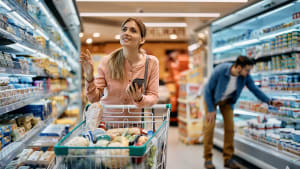 Femme souriante fait les courses avec un chariot plein.