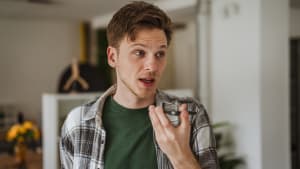 Jeune homme enregistrant un message vocal sur un smartphone � l'int�rieur