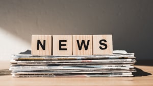 Des lettres NEWS posées sur une pile de journaux.