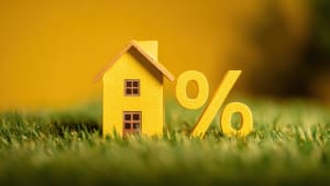 Maison jaune miniature et symbole de pourcentage sur herbe verte.