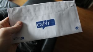 caf.fr, a hand holding an envelope with a partial view of the logo caf.fr Caisse d'Allocation Familiale on it. Translation of French: family allowance fund.