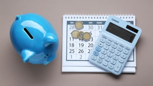 Un calendrier, une tirelire et une calculatrice sur fond gris