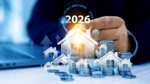 Main posant sur pi�ces, maisons et fl�ches repr�sentant croissance immobili�re 2026.