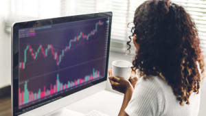 R�ussite d'une jeune femme d'affaires afro-am�ricaine, trader, qui �change des graphiques de march� boursier, vend et ach�te avec des graphiques financiers et des donn�es sur son ordinateur de bureau � la maison.