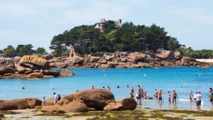 Brittany, France. Des personnes non reconnaissables se baignent et se détendent sur la plage avec une vue sur le château de la Côte de Granit Rose près de Ploumanach. Vacances en famille sur fond de Côtes d'Armor.