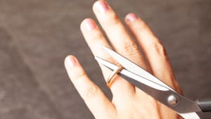la main d'une femme coupe une bague de fiançailles avec des ciseaux