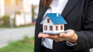 Une main tient une petite maison miniature, fond flou.