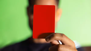 Une main tient un carton rouge devant un fond vert.
