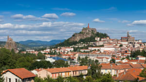 Ville avec collines, statue, église, toits rouges et ciel bleu. Puy-en-Velay