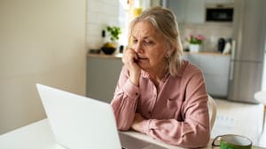 Une femme âgée inquiète devant son ordinateur portable dans sa cuisine.