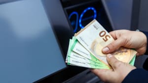 Des mains tenant divers billets de banque devant un distributeur automatique, pr�sentant le processus de retrait d'argent avec un affichage num�rique et des boutons �clair�s en arri�re-plan