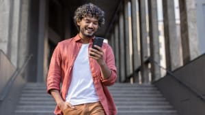 Un jeune debout près d'un bâtiment, la main dans la poche et utilisant un téléphone portable.