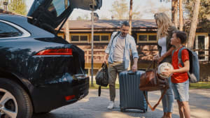 Une famille range des bagages dans le coffre d'une voiture.