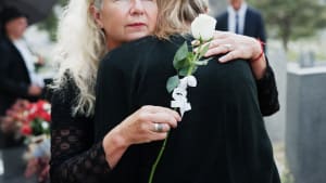 Femme, étreinte et funérailles avec rose pour les condoléances, le respect ou le deuil ensemble dans un cimetière. Personne féminine, famille et étreinte avec empathie ou chagrin pour l'adieu, l'enterrement ou la cérémonie dans le cimetière.