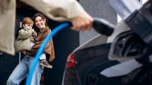 IUne femme debout portant un enfant pendant qu'une autre personne charge une voiture �lectrique.