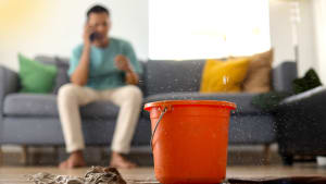 Un seau recueille de l?eau qui fuit du plafond, avec en fond, un homme au téléphone.