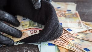 Des mains dans des gants de cuir noir mettant des billets dans un sac.