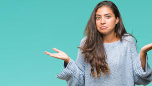 Jeune belle femme arabe portant un pull d'hiver sur un fond isolé, expression perplexe et confuse avec les bras et les mains levés. Concept de doute.