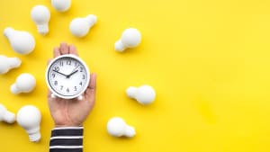 Quelqu'un tient une horloge sur fond jaune avec des ampoules tout autour.
