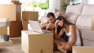 Un homme et une femme l'air inquiet, consultant un ordinateur portable et entourés de cartons de déménagement.