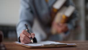 Main d'affaires tenant un stylo et signant un contrat plac� sur un presse-papiers, tout en portant �galement des livres de droit, symbolisant l'expertise juridique, l'accord et les documents officiels.