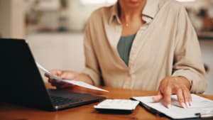 Femme, mains et document dans un appartement avec un ordinateur portable, une calculatrice et une administration pour les factures de services publics. Personne, paperasse et ordinateur à la maison avec planification financière, dépenses domestiques et déclaration de revenus.