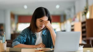 Jeune femme stressée en étudiant avec un ordinateur portable à la bibliothèque, étudiante débordée se préparant pour les examens, pression académique et santé mentale