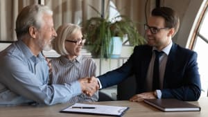 Couple de personnes âgées heureux serrant la main de l'agent immobilier, du notaire, de l'avocat. Homme et femme mûrs achetant une maison, une assurance maladie, consultant un professionnel, serrant la main sur les documents.