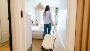 Une femme entrant dans une chambre avec une valise à roulettes.