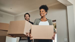 Couple heureux, immobilier et emménagement avec des cartons pour rénovation, investissement ou réinstallation dans une nouvelle maison. Homme et femme interraciaux, propriétaire agent immobilier, portant une boîte dans la maison, déménagement ou prêt immobilier ensemble.