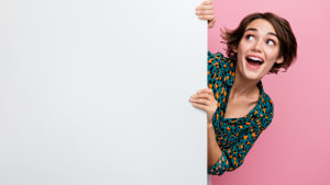 Portrait de femme ravie aux cheveux au carré portant une blouse imprimée tenant un mur blanc regardant l'offre d'un espace vide isolé sur fond rose