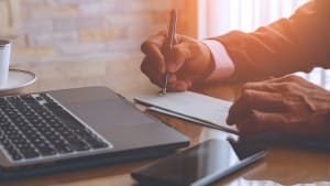 Un homme d'affaires écrit et signe un chèque avec un ordinateur portable sur la table en bois d'un bureau moderne à domicile.
