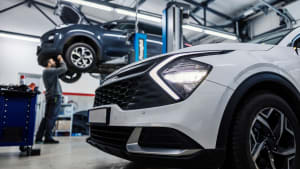 Une voiture au premier plan avec un mécanicien automobile réparant une autre voiture en arrière-plan.