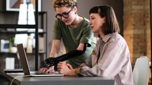 Une jeune femme avec une prothèse au bras pointant un ordinateur portable.