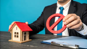 Homme en costume, maison miniature, symbole d?interdiction, dossier.