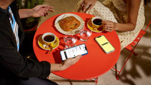 Deux personnes prennent un café avec viennoiserie, téléphones présents.