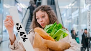 Une femme examine un ticket tout en tenant des légumes et une baguette.